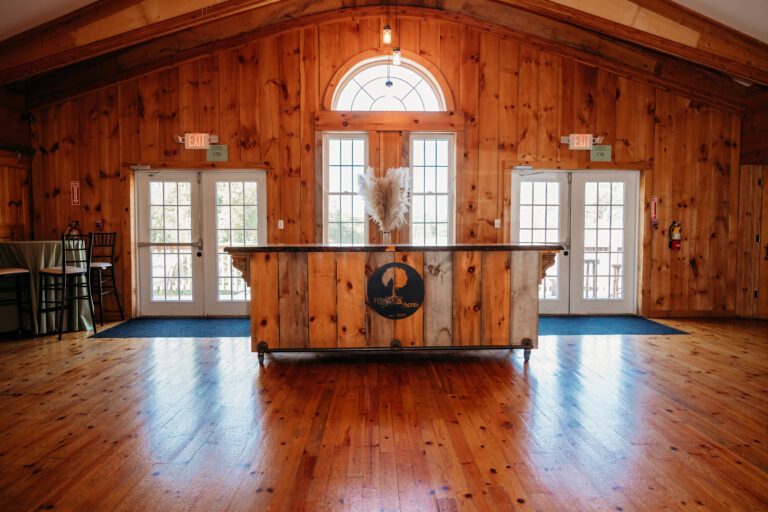 Rustic wooden lodge lobby with a central reception desk beneath an arched window and polished hardwood floors.