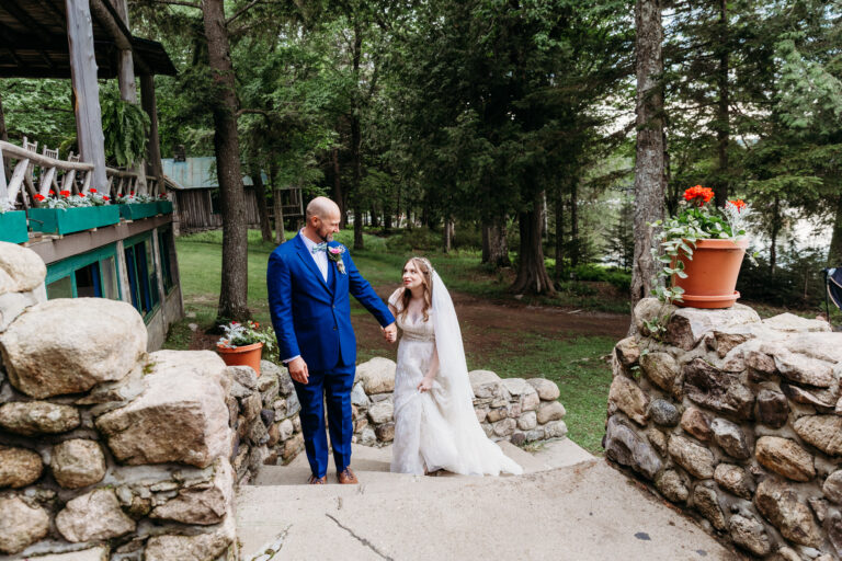 A man in a blue suit and a young girl in a white dress walk hand in hand down stone steps in a garden.