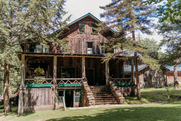 Rustic two-story wooden house with a large front porch and surrounding trees.