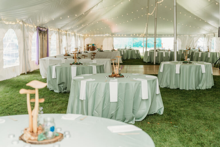 Reception setup inside a large white tent with round tables covered in mint-green tablecloths, centerpieces, and string lights.