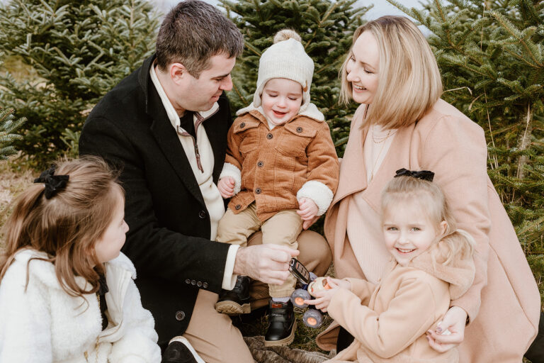 A family of five wearing warm coats outdoors in a wooded area, smiling and enjoying time together.