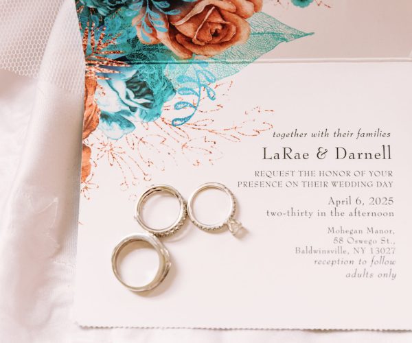 Wedding invitation with floral design and three rings displayed. Event at Mohegan Manor, Baldwinsville, NY, on April 6, 2025, at 2:30 PM.