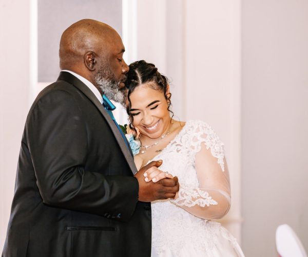 Two people are happily dancing, wearing formal attire. One person is in a black suit, the other in a white lace dress.